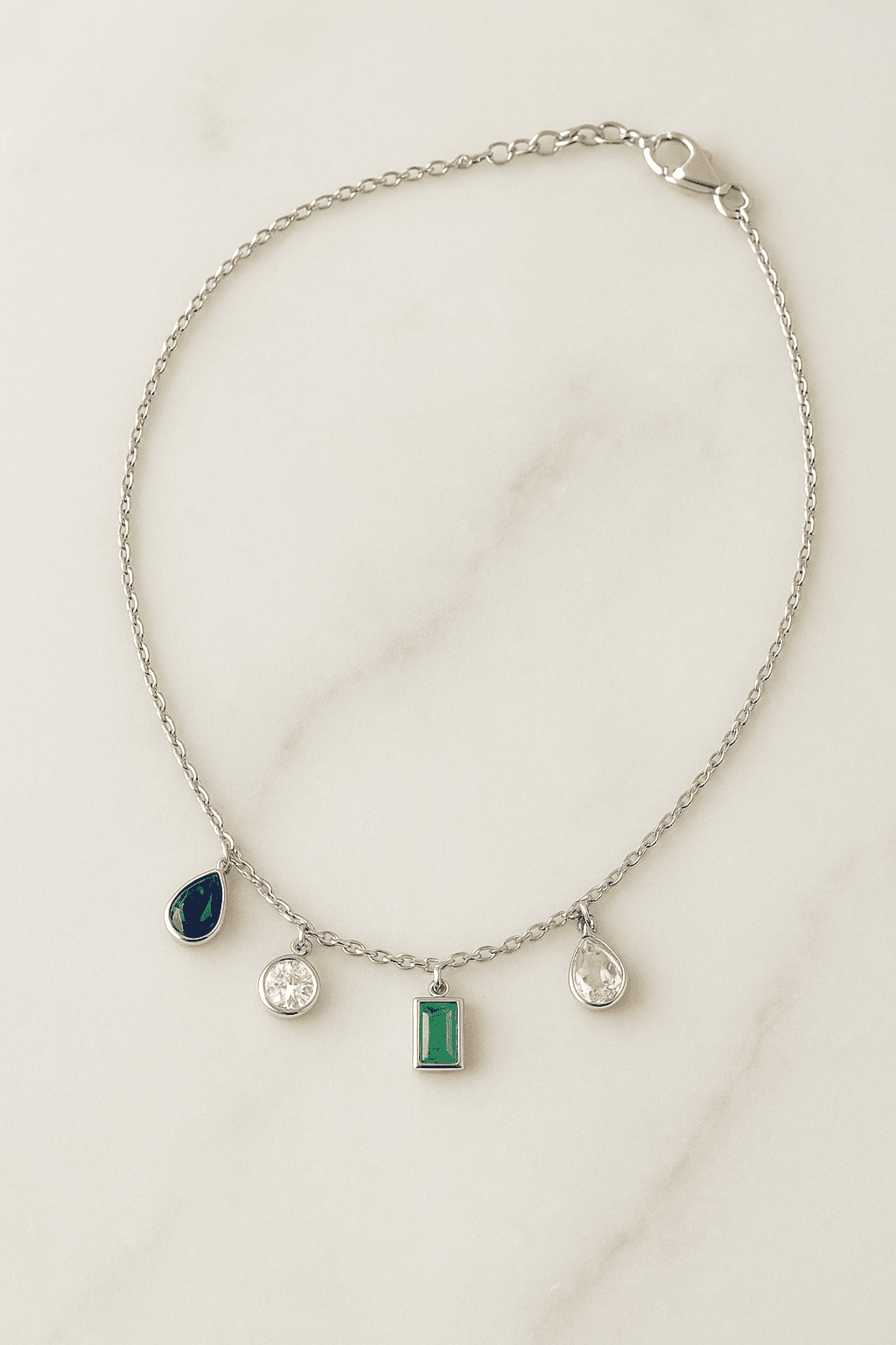 Silver charm necklace with gemstone charms including sapphire, emerald, and diamonds