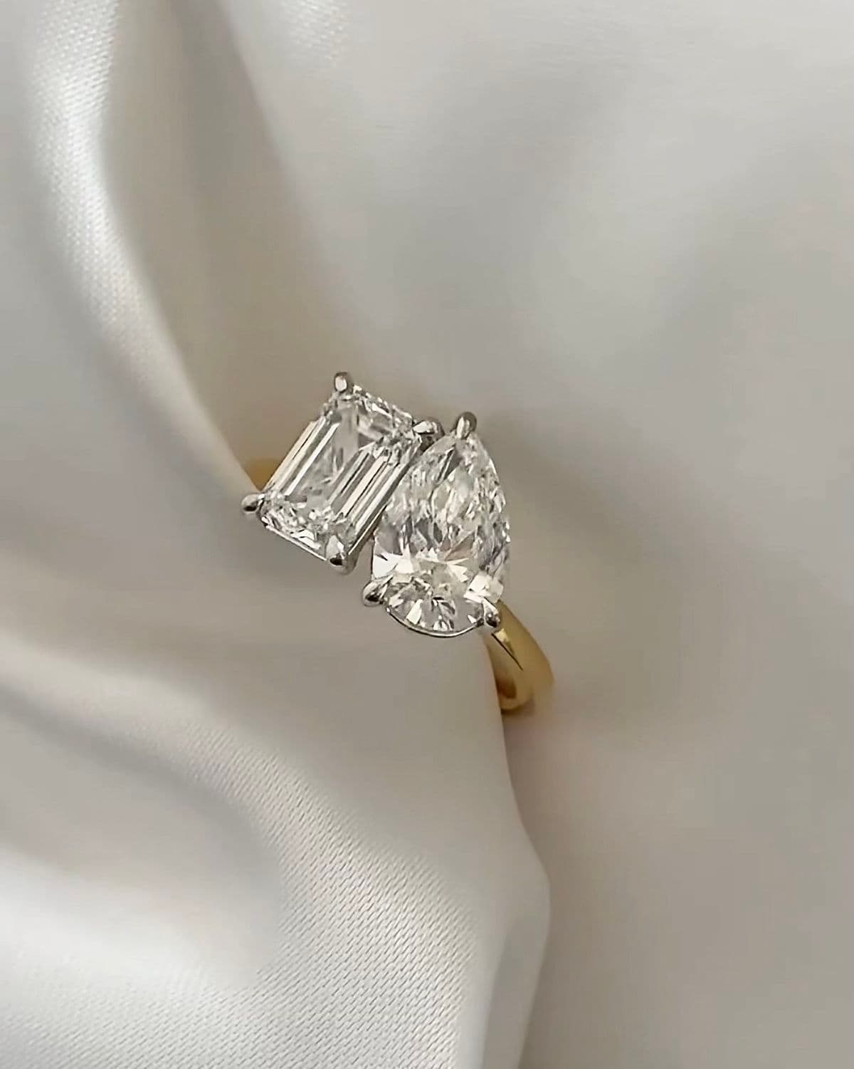 Toi et moi engagement ring with emerald cut and pear diamond in yellow gold setting on white satin